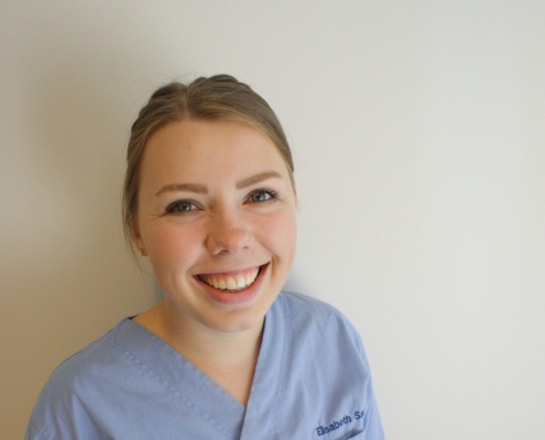 Bilde av en smilende Elisabeth Sælø osteopat i lyseblå arbeidsklær.
